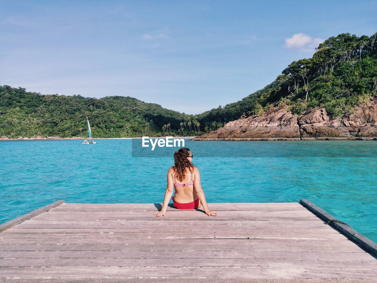 Rear view of woman sitting by sea against sky