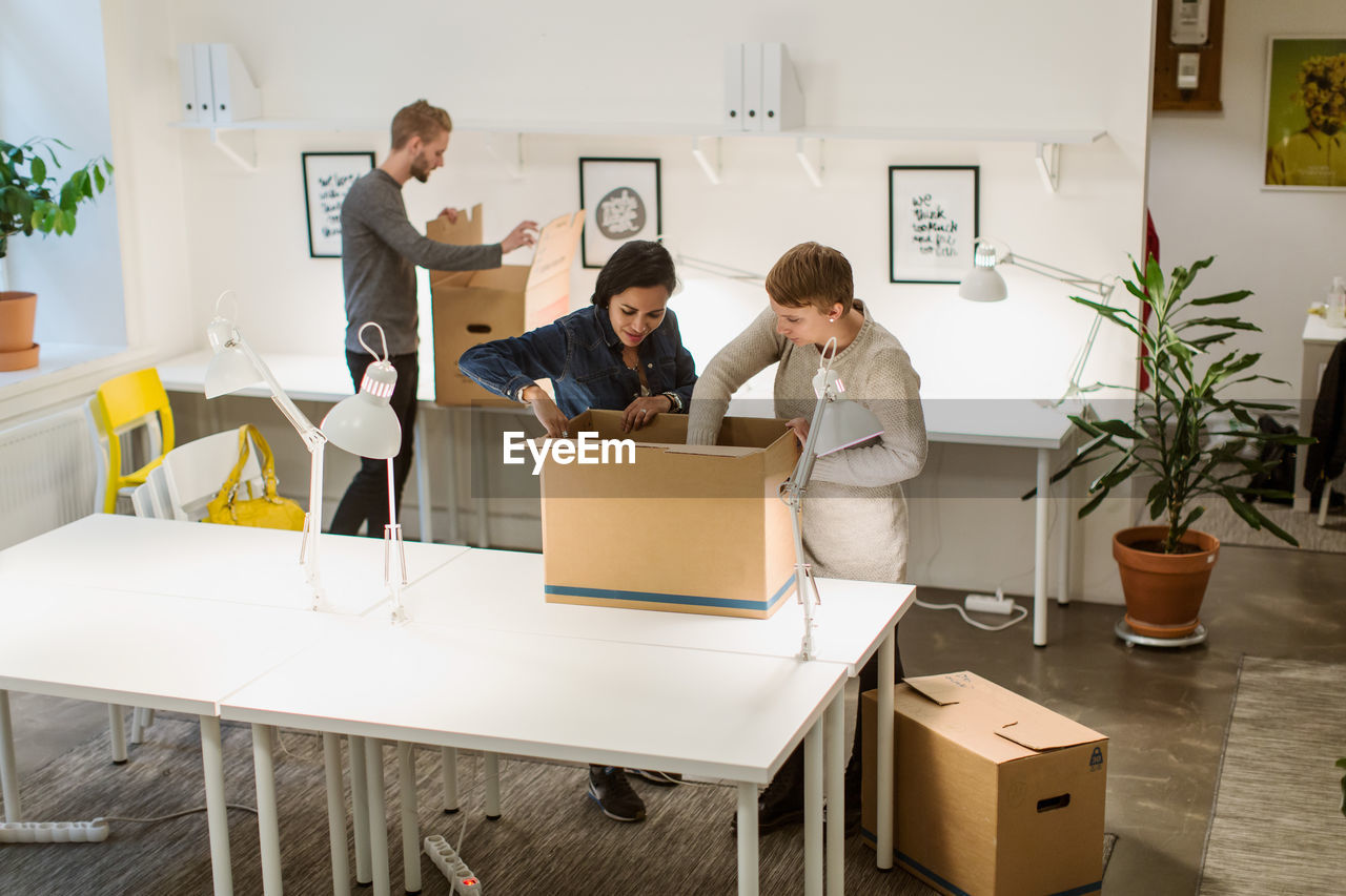 High angle view of multi-ethnic business coworkers opening cardboard boxes at creative office