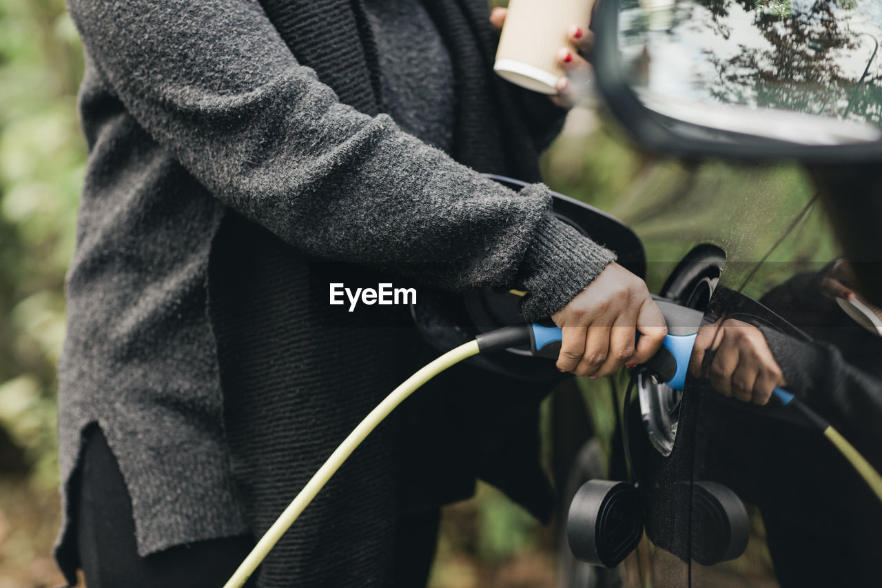 Midsection of mid adult woman charging electric car