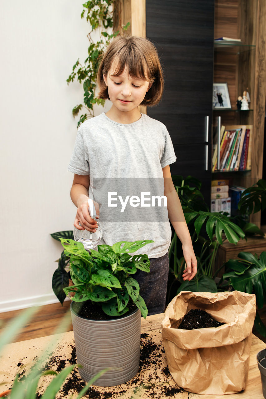 A teenage girl sprays home flowers from a spray bottle at home. house plant care. hobby 