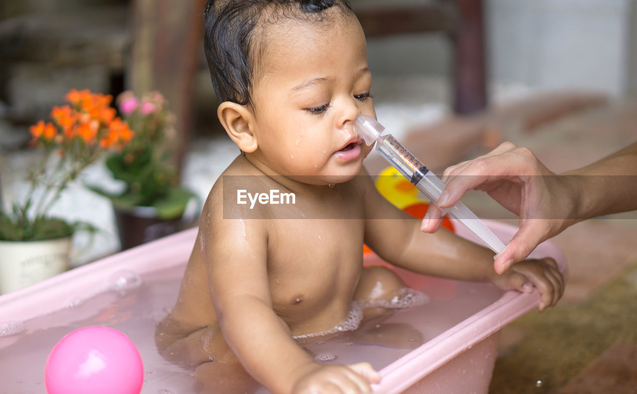 Cropped hand of woman cleaning baby nose using syringe at home