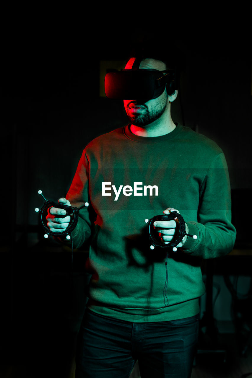 A young man plays with virtual reality equipment in a dark room