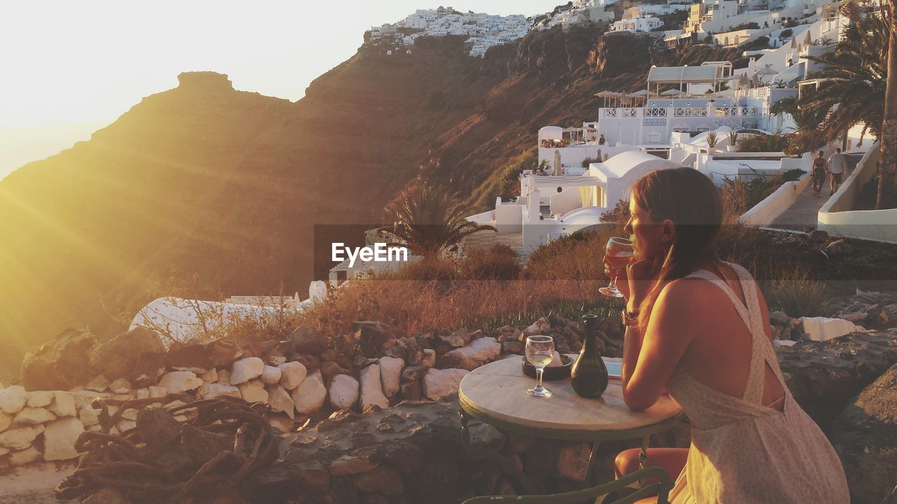 Woman holding wineglass while sitting by table during sunset