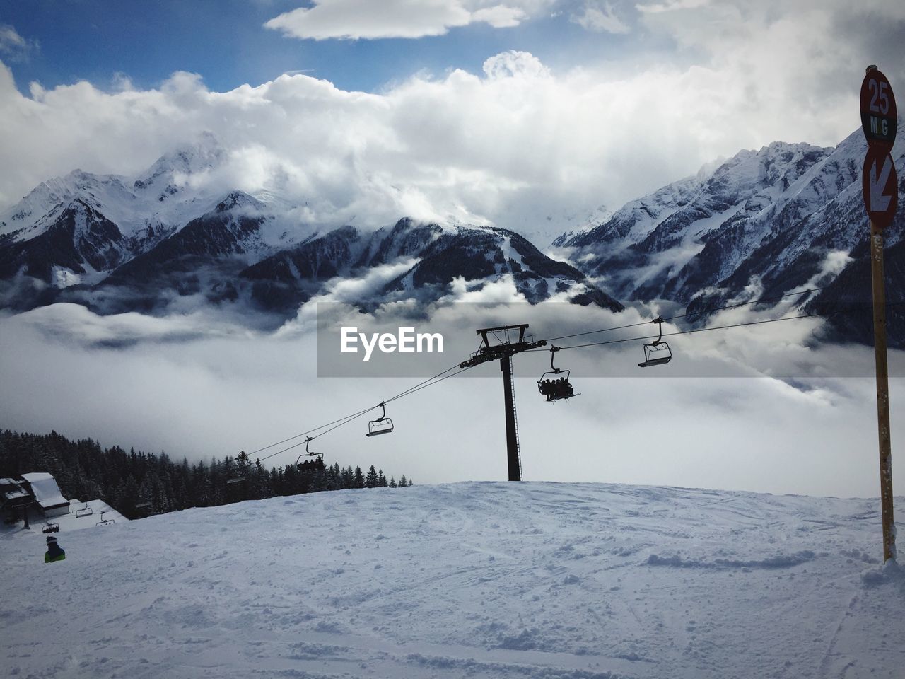 Ski lift over snowy hill against snowcapped mountains and cloudy sky