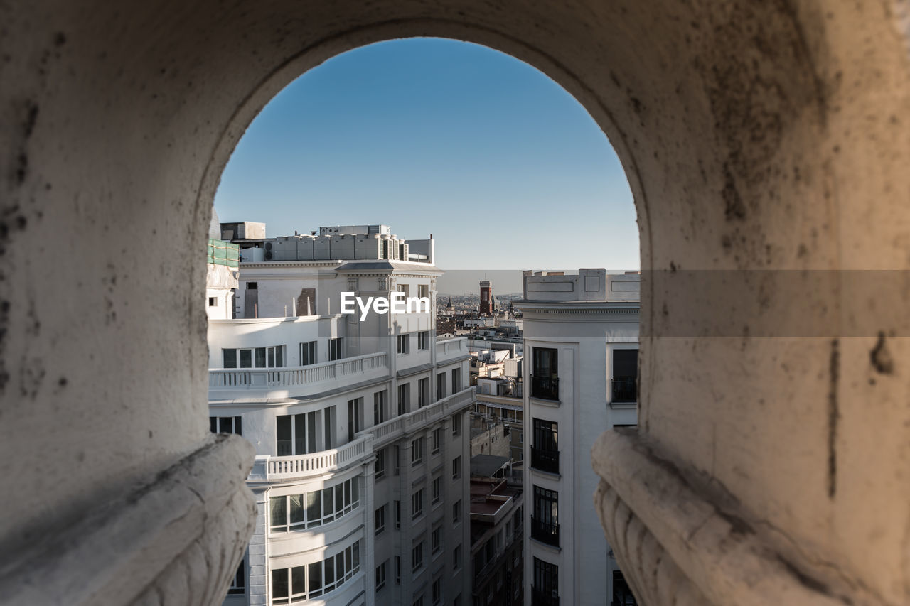 Buildings in city against clear sky seen through arch