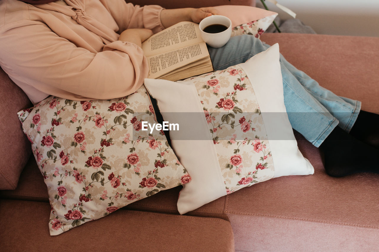 Low section of woman reading book sitting on sofa at home