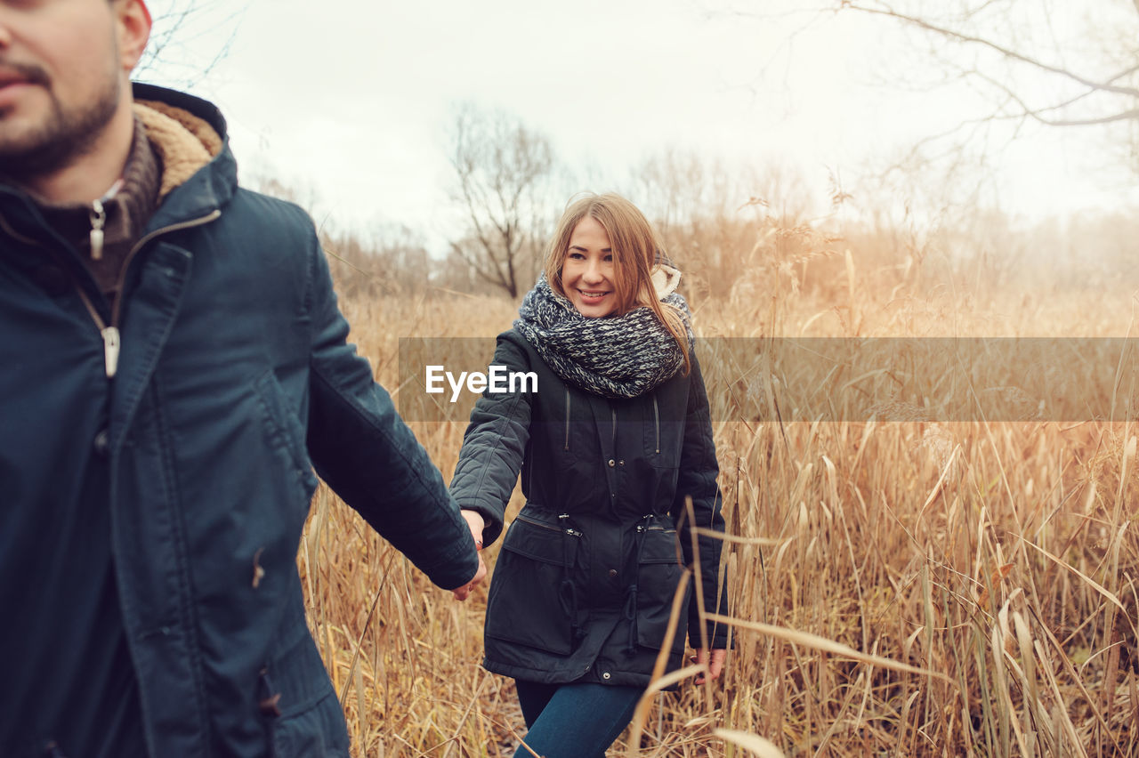 Man holding hands of woman while walking on grassy field during winter