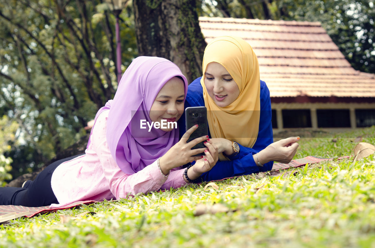 Friendship and happiness concept. portrait of smile young muslimah laying on grass at city park