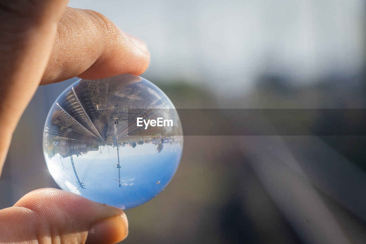 blue, hand, holding, close-up, one person, sphere, macro photography, focus on foreground, reflection, glass, light, nature, crystal ball, finger, outdoors, globe - man made object, transparent, day, water, adult, single object, ball