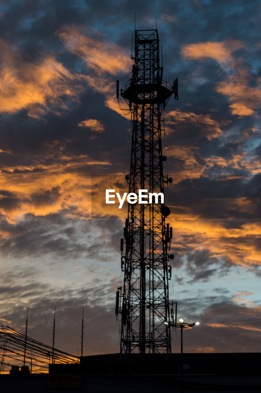 Low angle view of silhouette communications tower against cloudy sky during sunset