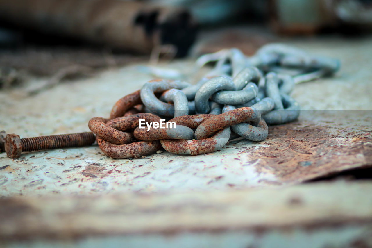 CLOSE-UP OF RUSTY METAL TIED UP ON CHAIN