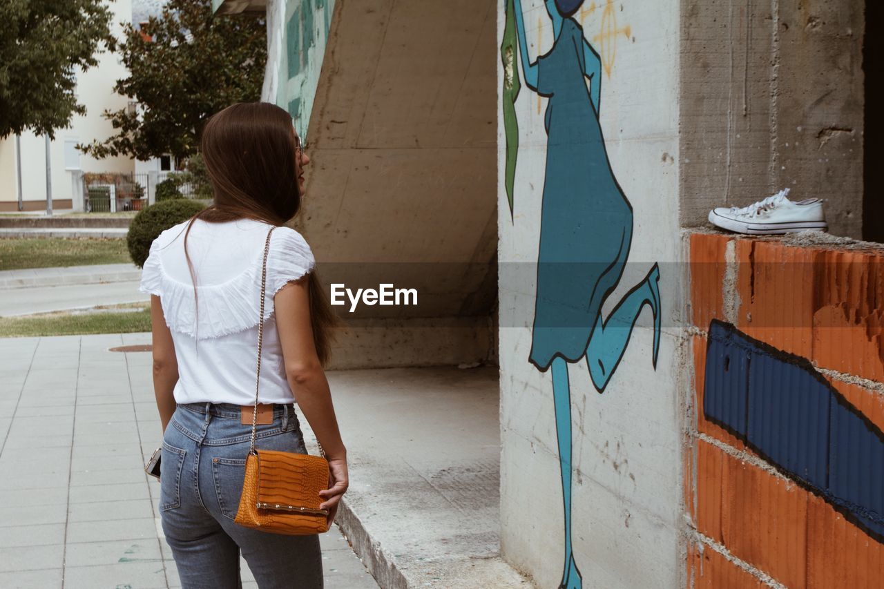 FULL LENGTH REAR VIEW OF WOMAN STANDING AGAINST WALL