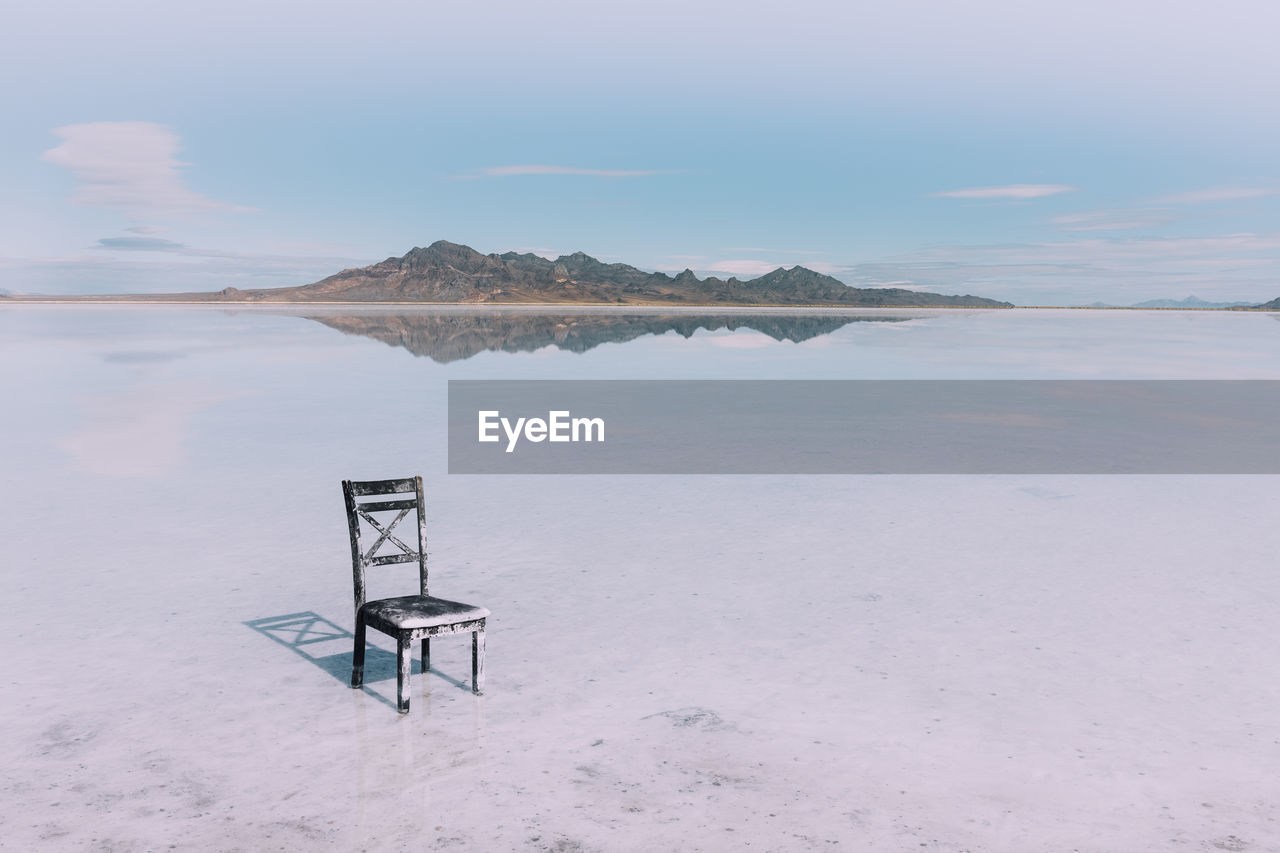 Empty chair on beach against sky