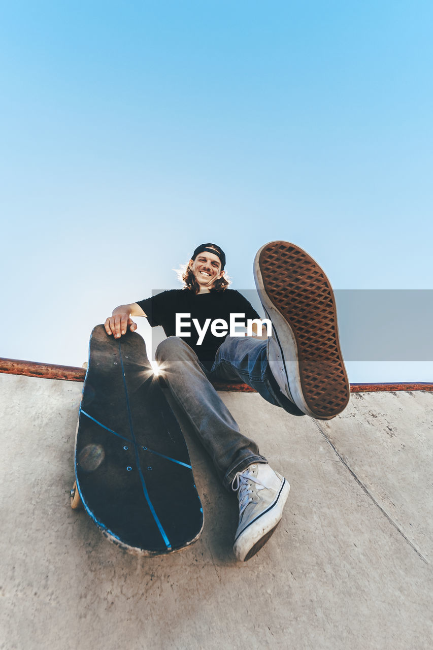 Happy man with skateboard sitting at skateboard park