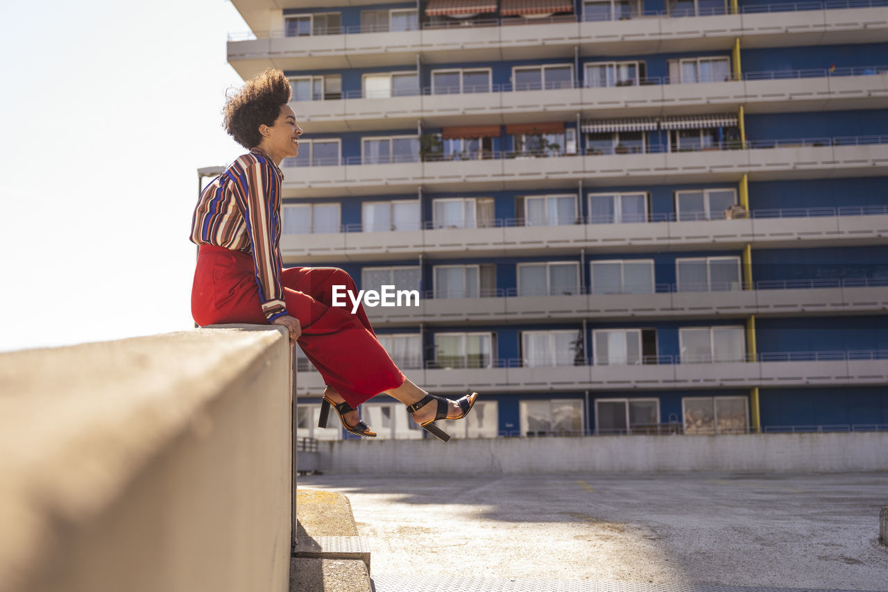 Smiling woman with tousled hair sitting on wall at parking deck