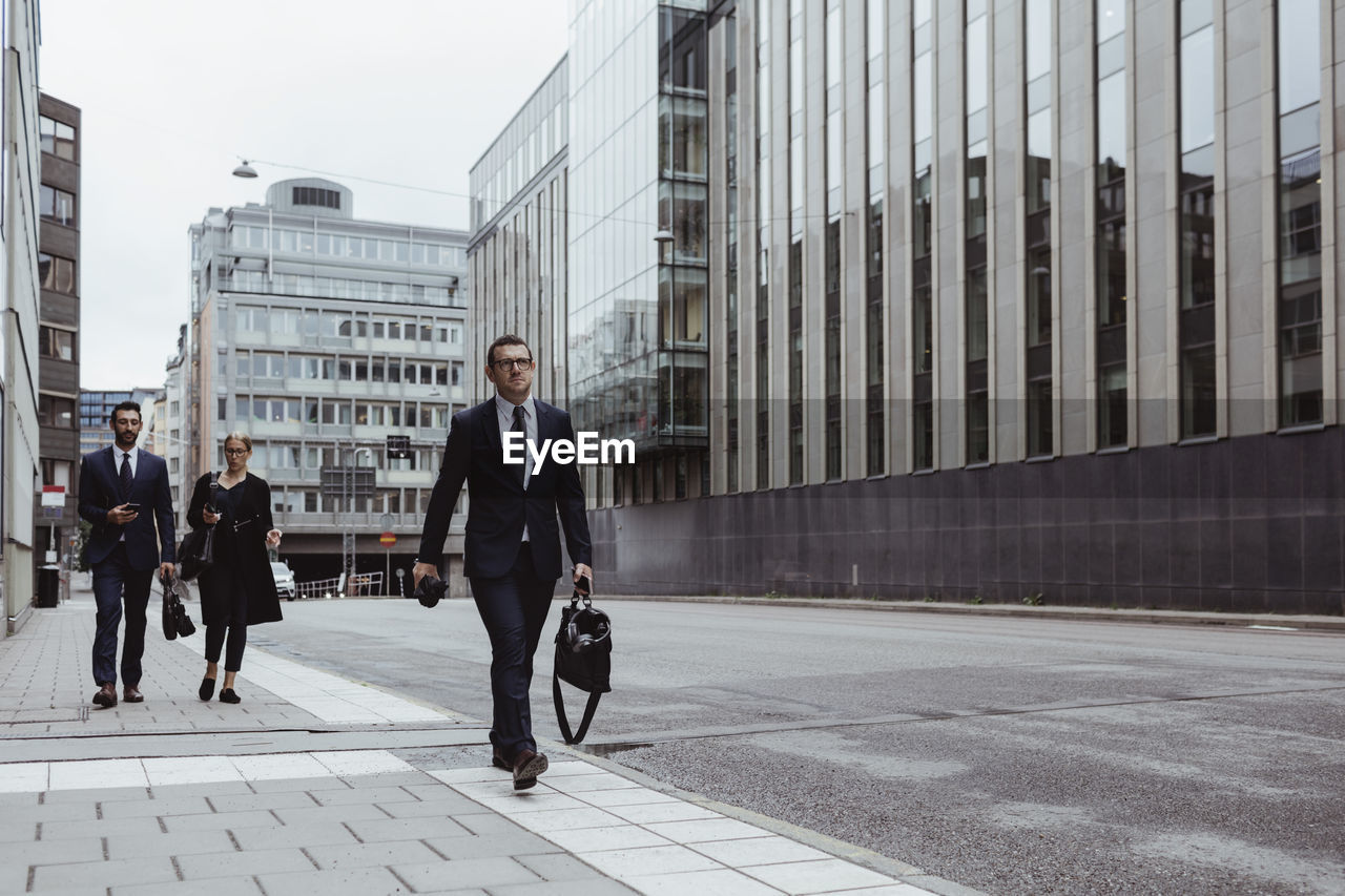 Male entrepreneur with bag walking ahead of coworkers in city