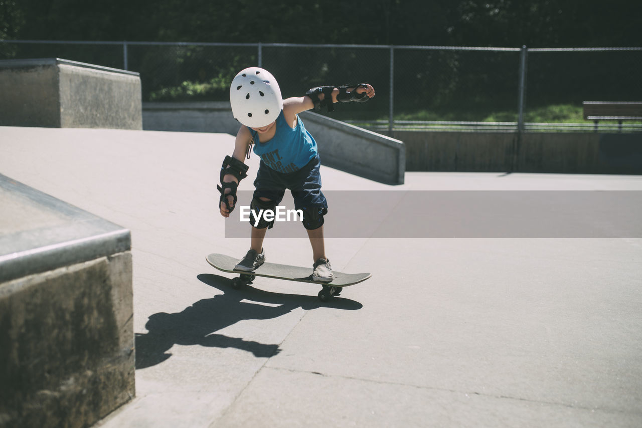 Full length of boy skateboarding at skateboard park during summer
