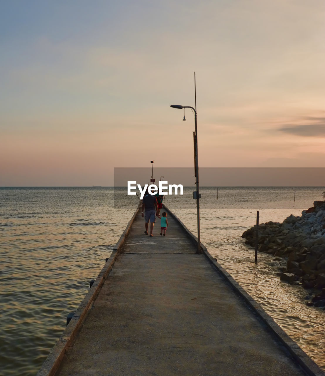 People walking on pier in sea against sunset sky