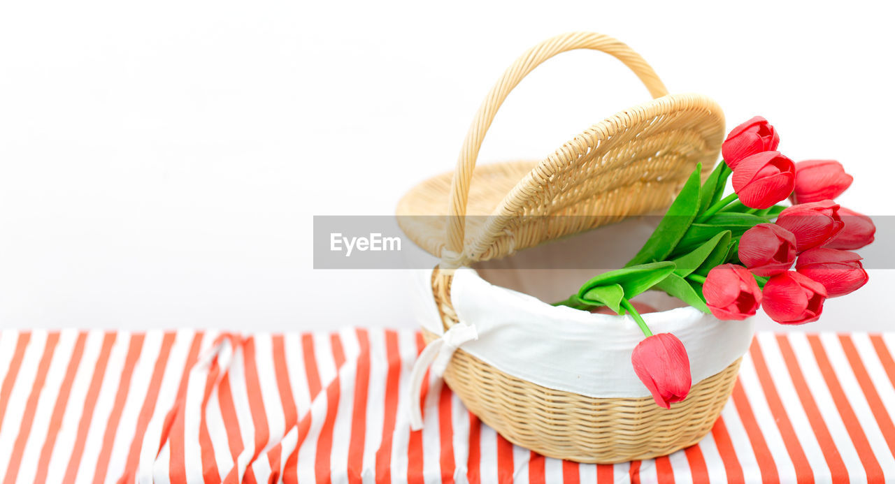 Close-up of red roses in basket on table against white background