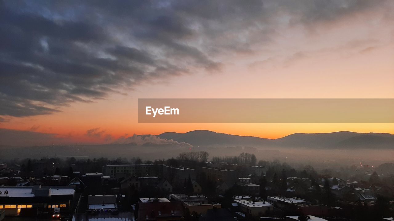 HIGH ANGLE SHOT OF TOWNSCAPE AGAINST ORANGE SKY