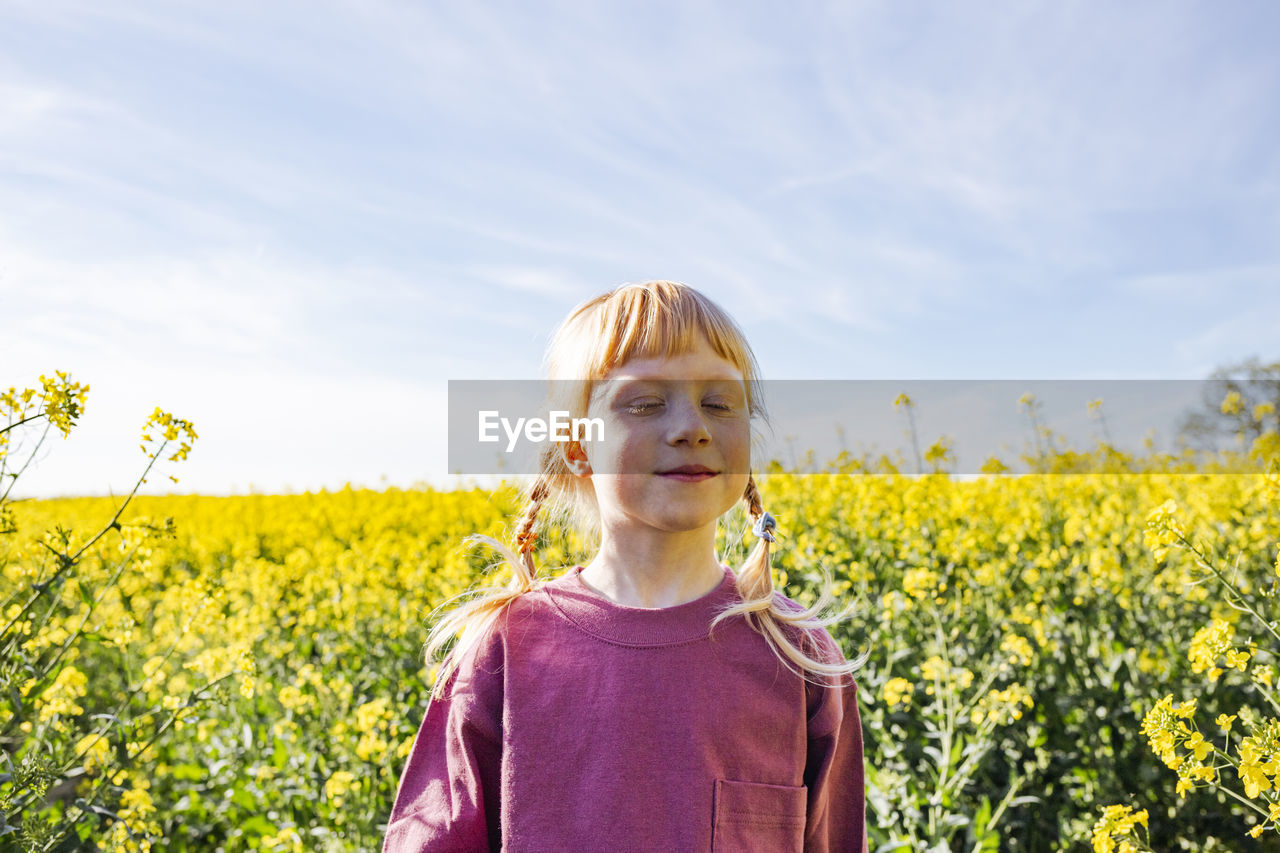 Smiling redheaded girl with eyes closed standing on rapeseed field