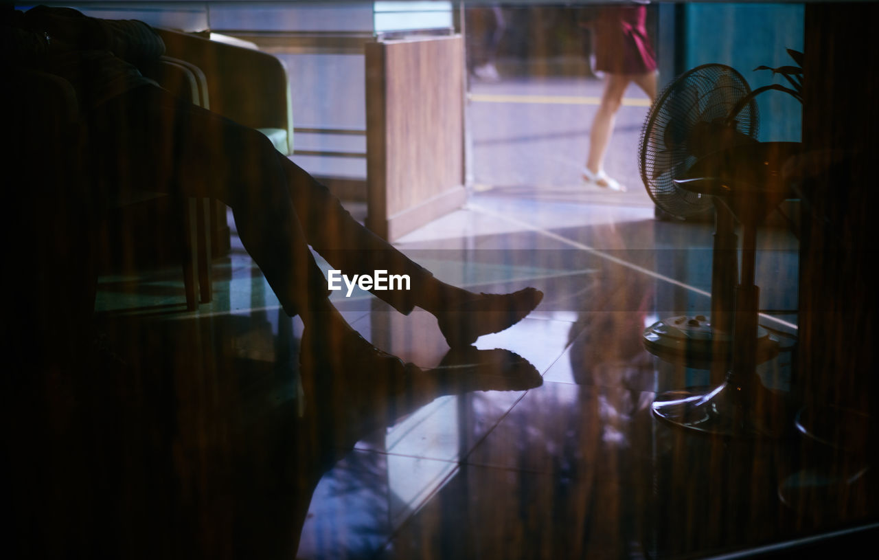 Low section of man sitting on chair seen through glass