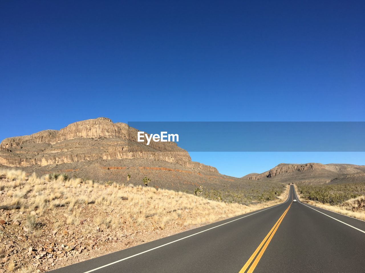 Empty road against clear blue sky