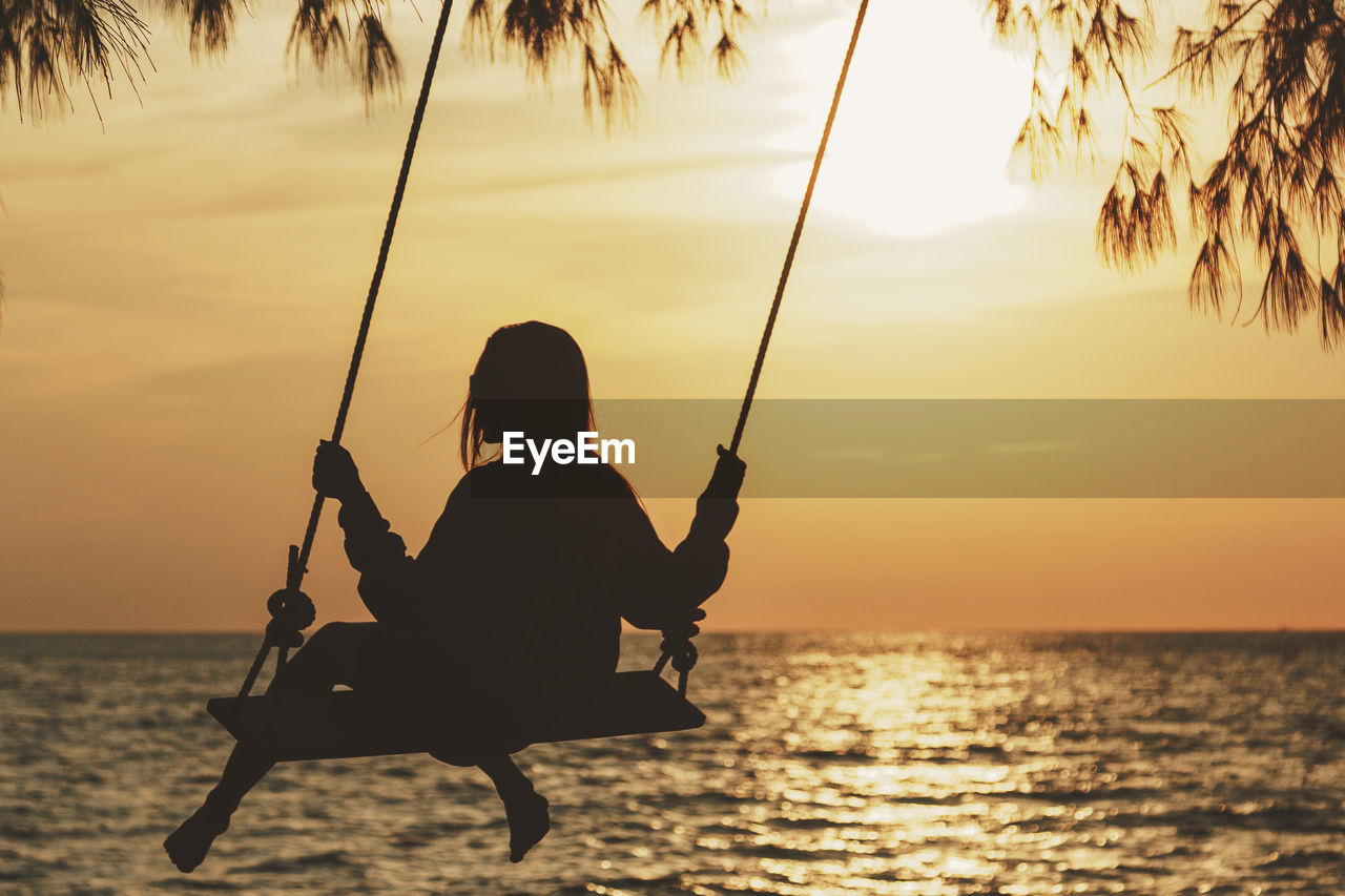 Silhouette woman swinging against sea during sunset