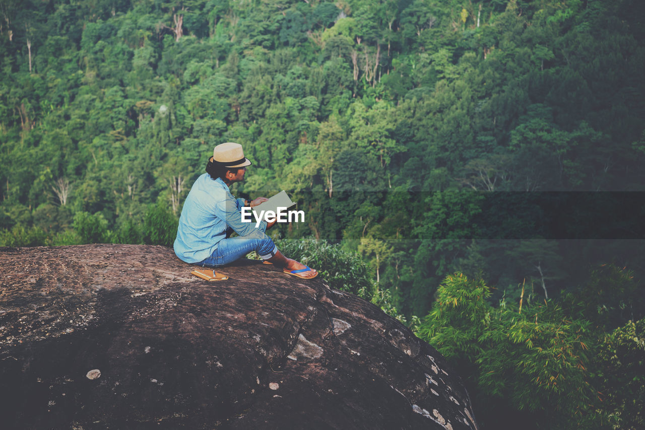 High angle view of man wearing hat sitting on cliff