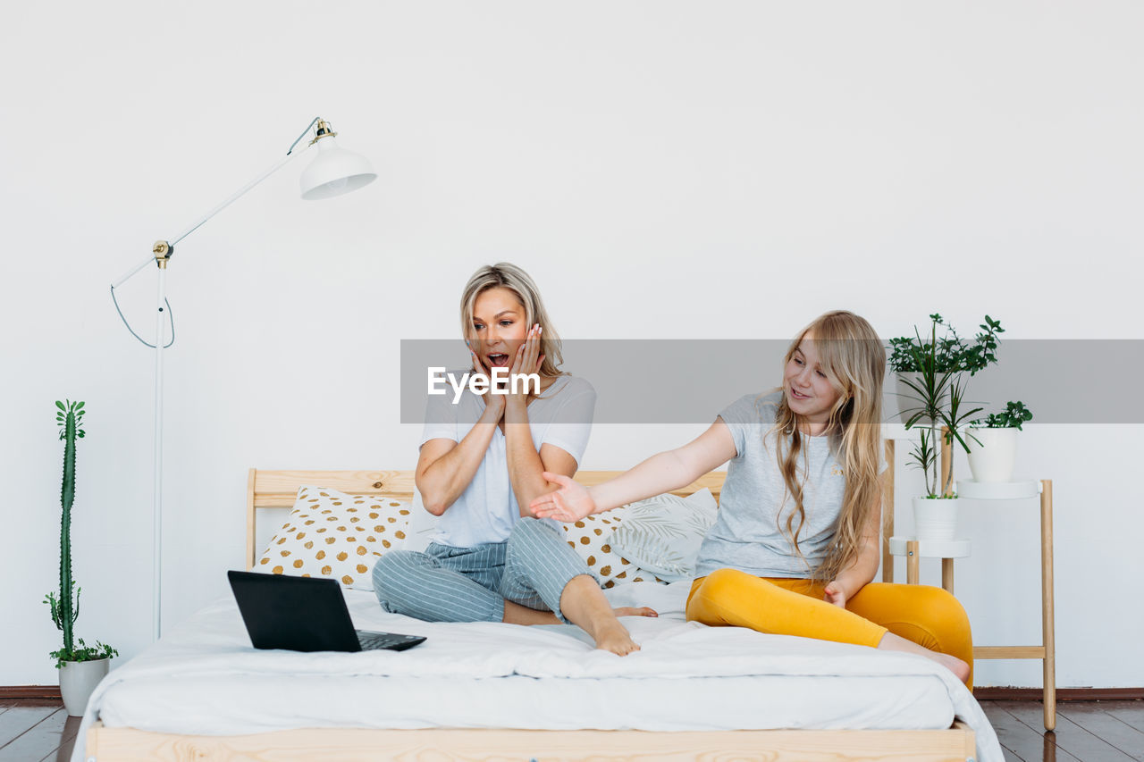 Smiling mother using laptop sitting with daughter on bed at home