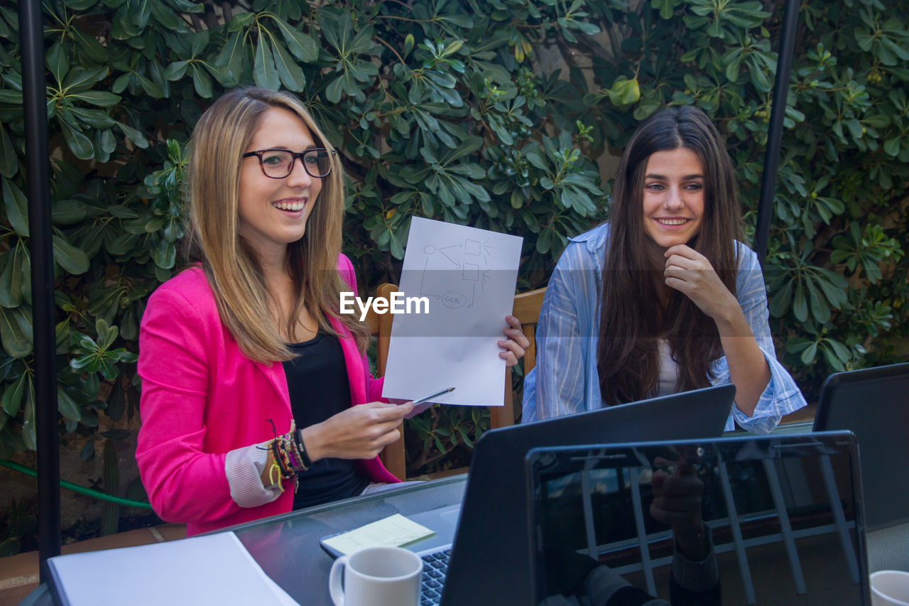 Smiling colleagues discussing over diagram against plants