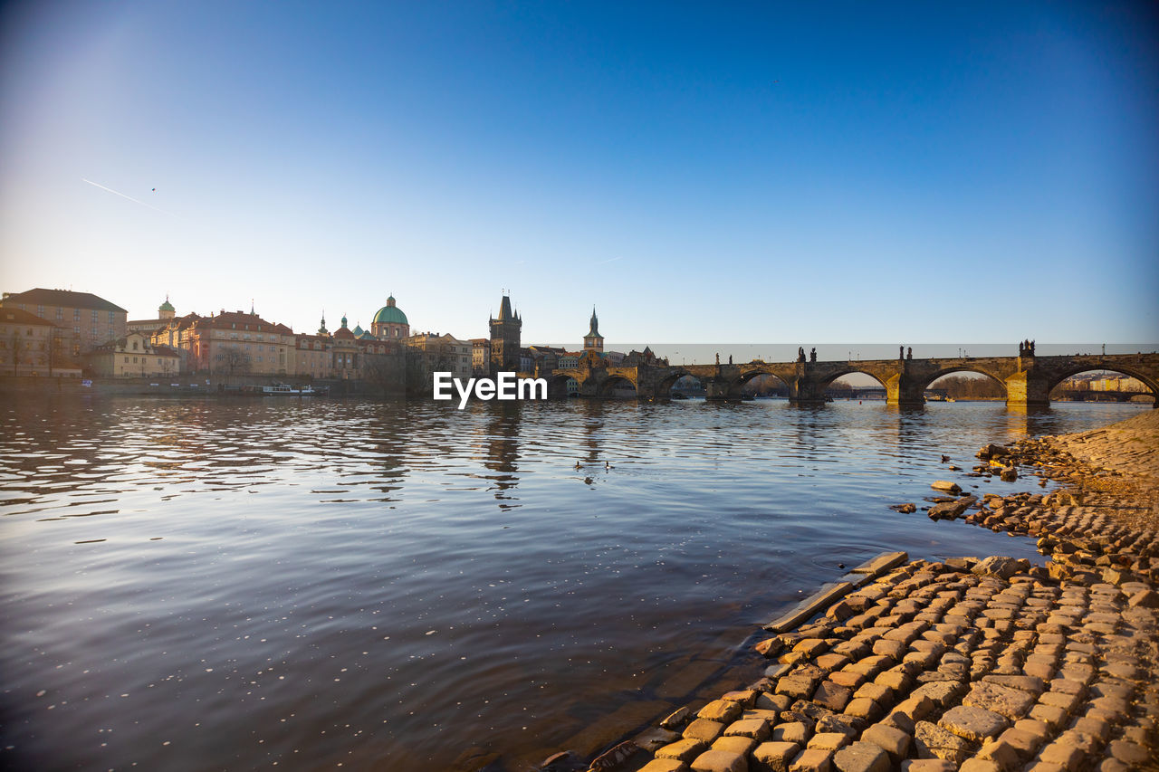 Bridge over river by buildings against clear sky