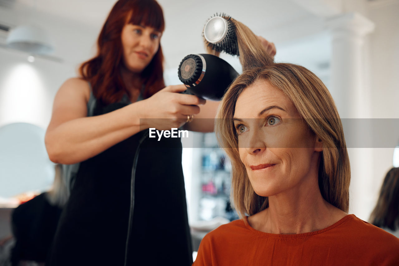 women, adult, indoors, hairdresser, two people, female, lifestyles, customer, young adult, body care, person, portrait, occupation, small business, clothing, smiling, hair salon, fashion, mirror, human face, holding, hairstyle, standing, business, focus on foreground