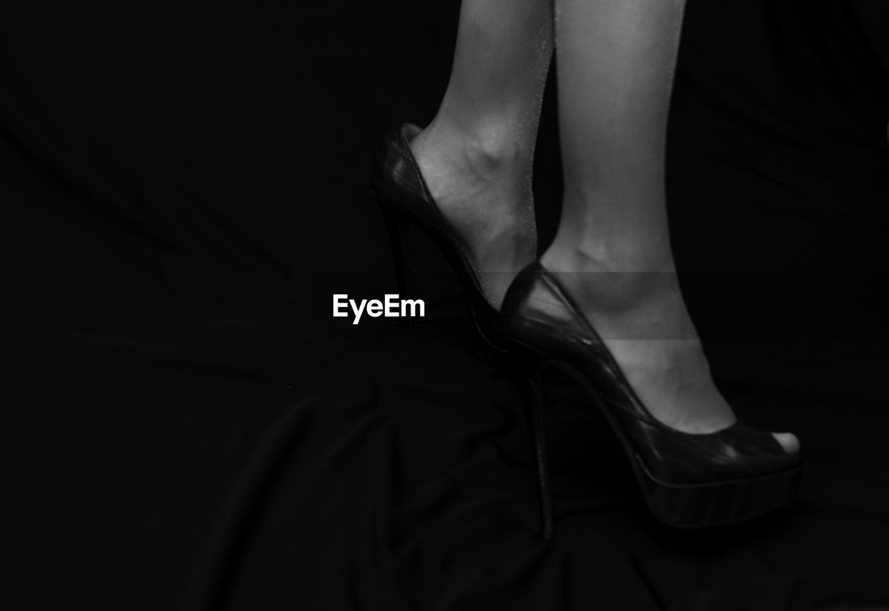 Low section of woman wearing high heels against black background