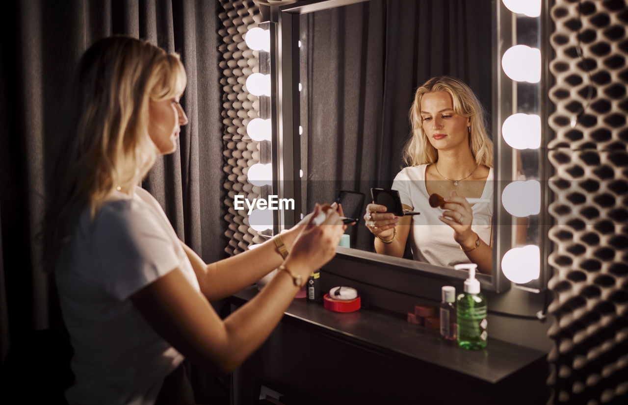 Young woman applying make-up in front of mirror