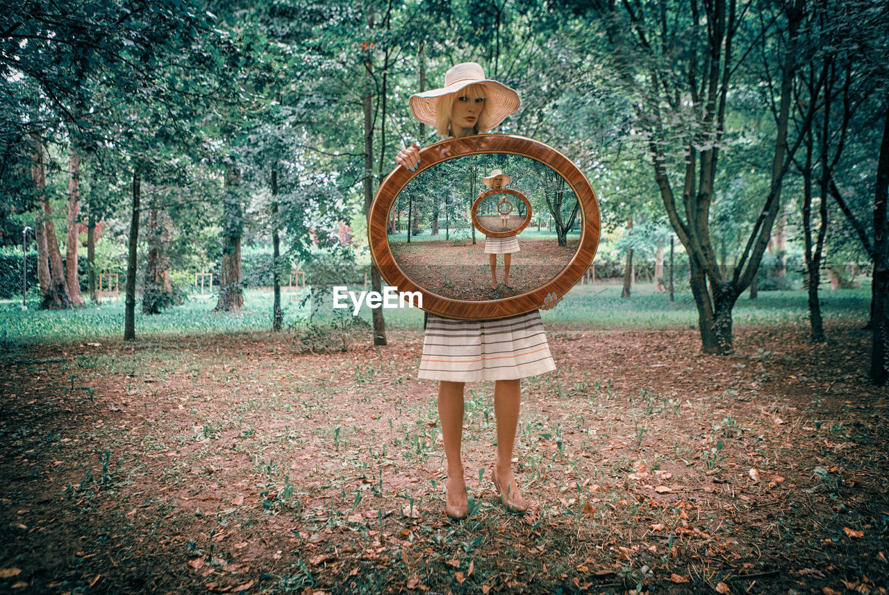 Portrait of woman holding mirror while standing in forest