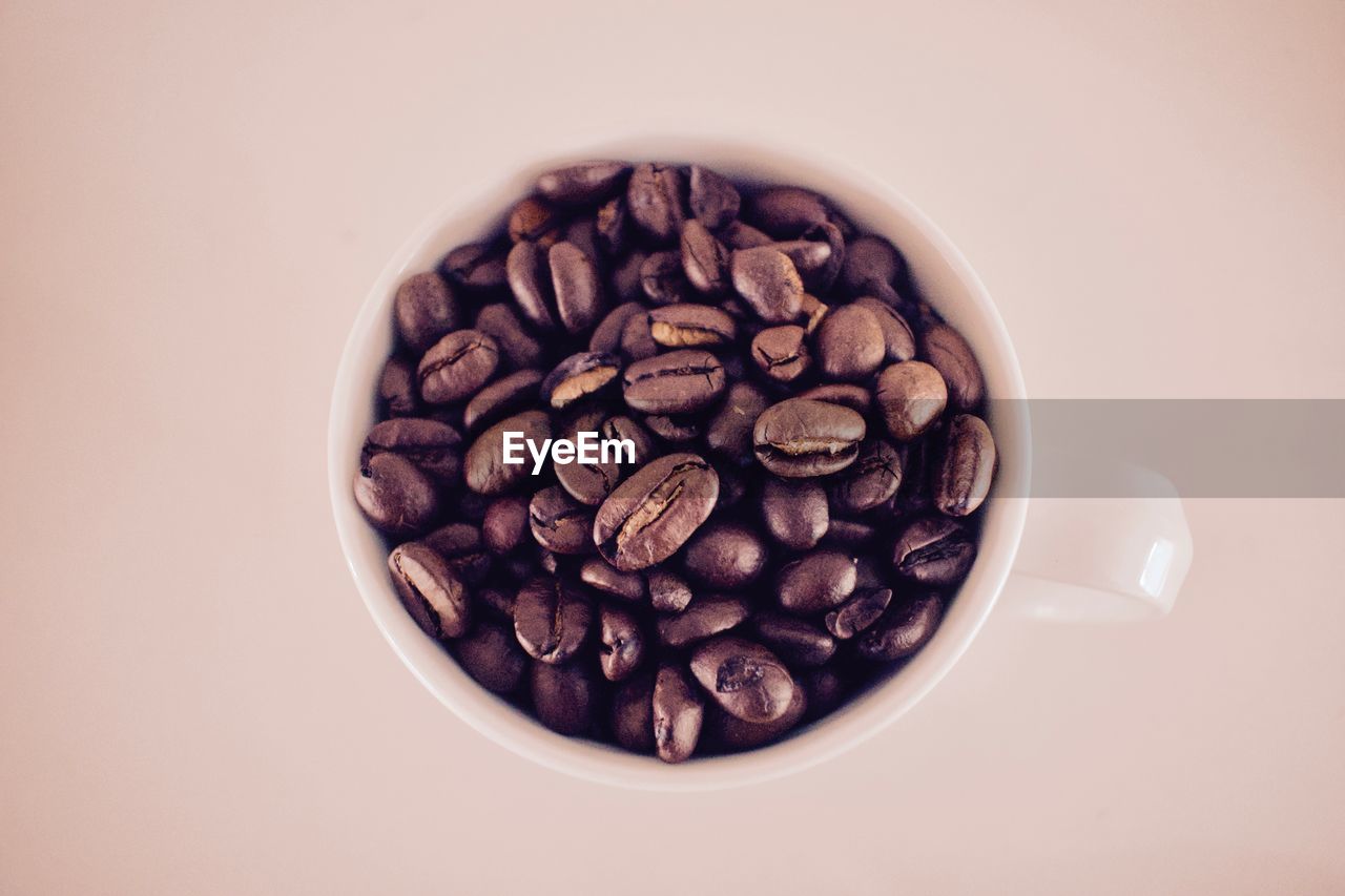 Close-up of roasted coffee beans in cup over colored background