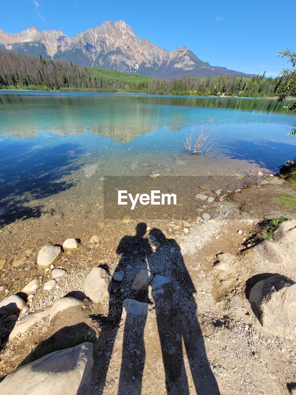 SHADOW OF MAN STANDING ON LAKE AGAINST MOUNTAINS