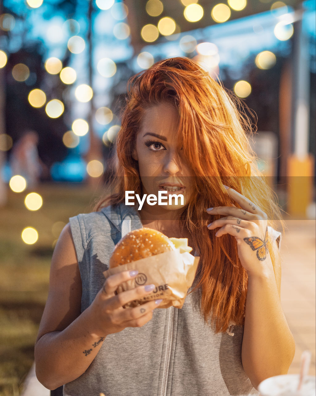 Portrait of woman holding burger in city at night