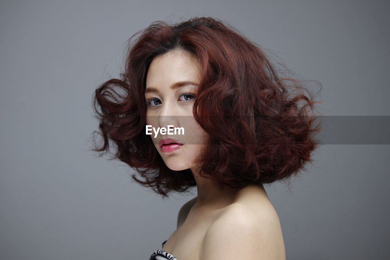 PORTRAIT OF YOUNG WOMAN AGAINST GRAY BACKGROUND