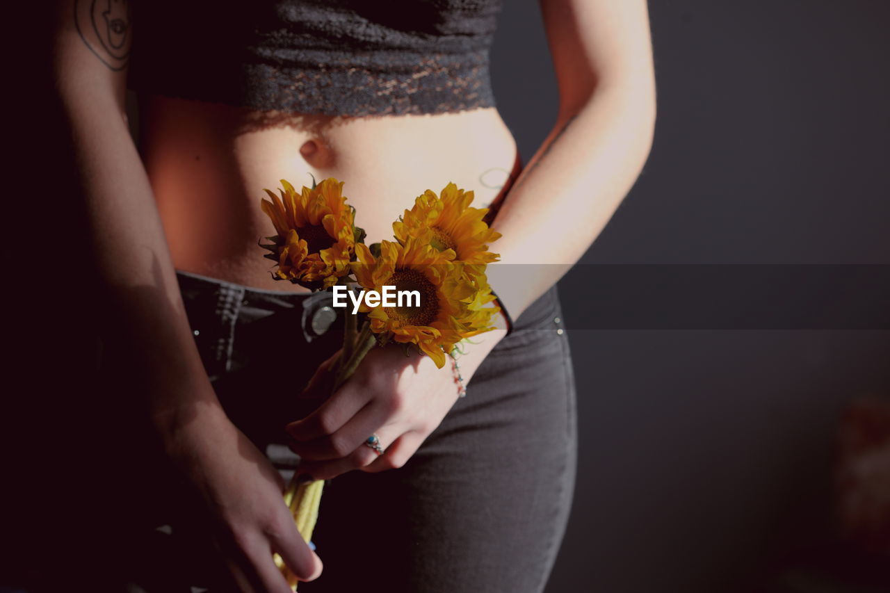 Midsection of woman holding sunflowers against wall