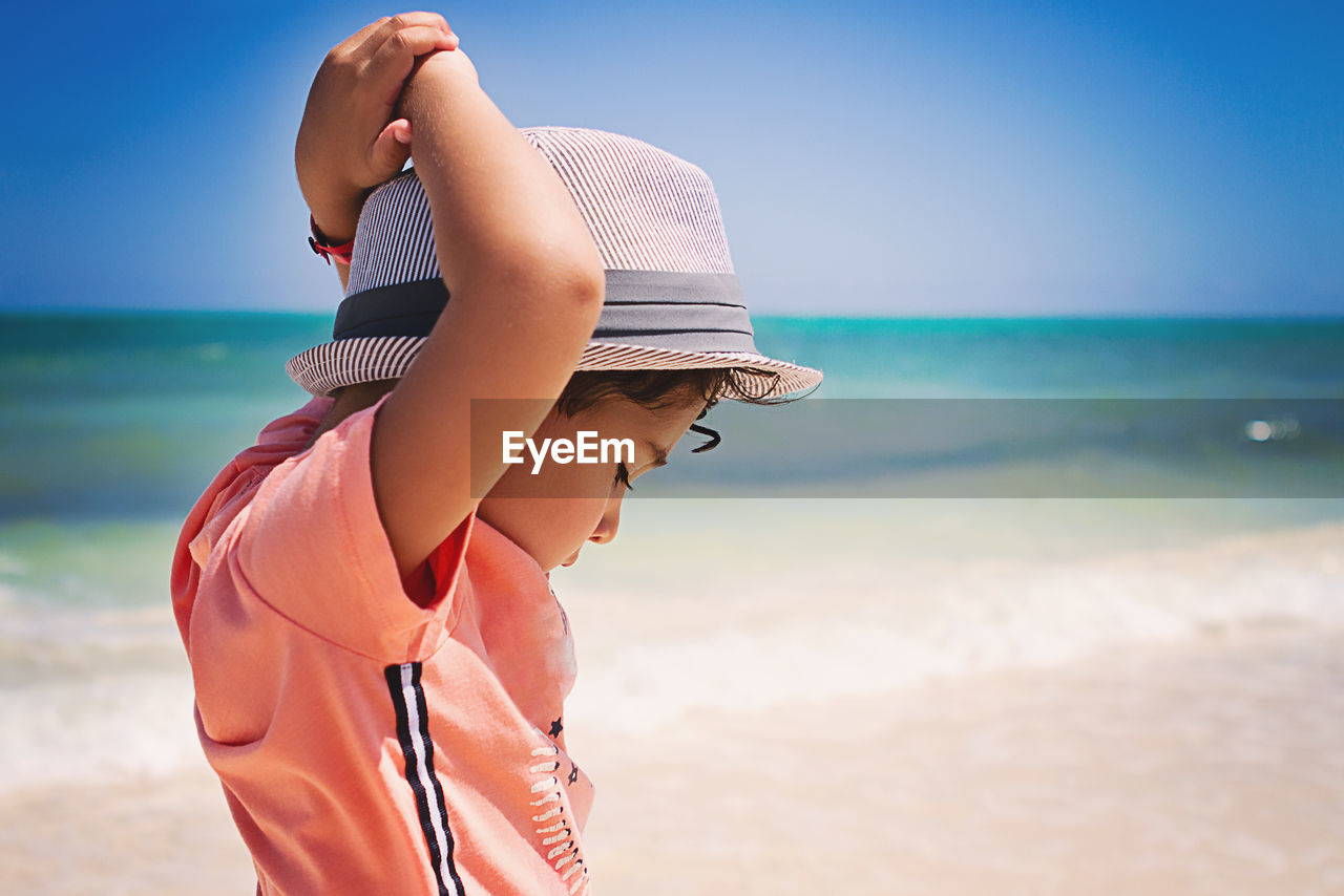 Little boy with curly hair looking down at a beach in the caribbean.