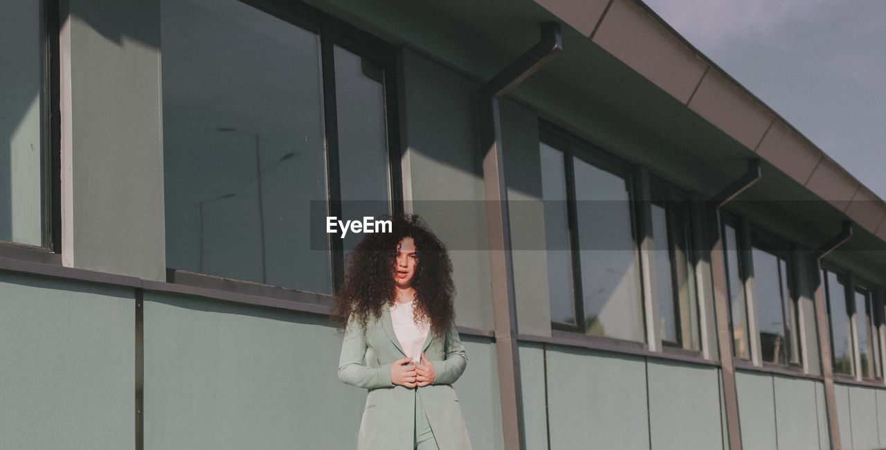 Portrait of woman with curly hair standing against building