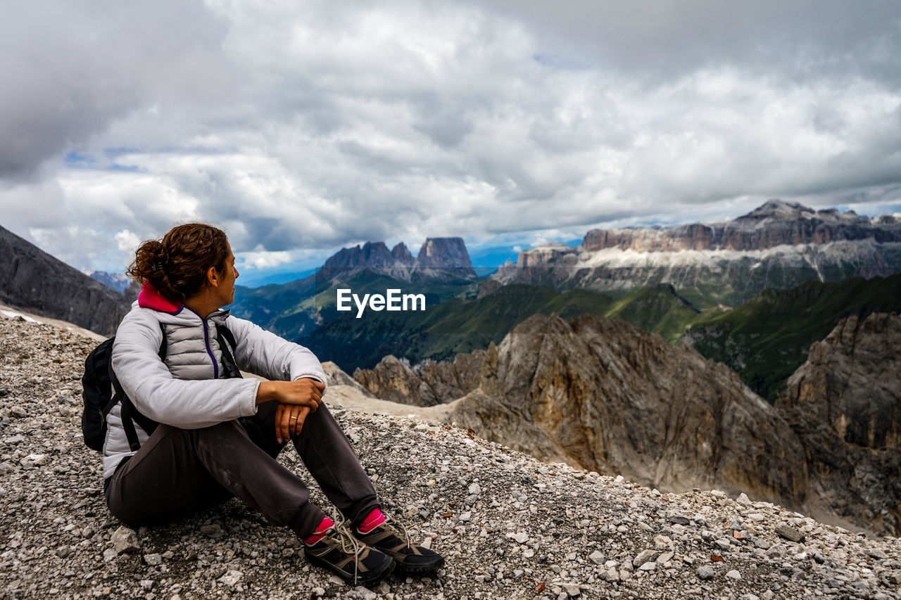 Man sitting on rock looking at mountains against sky