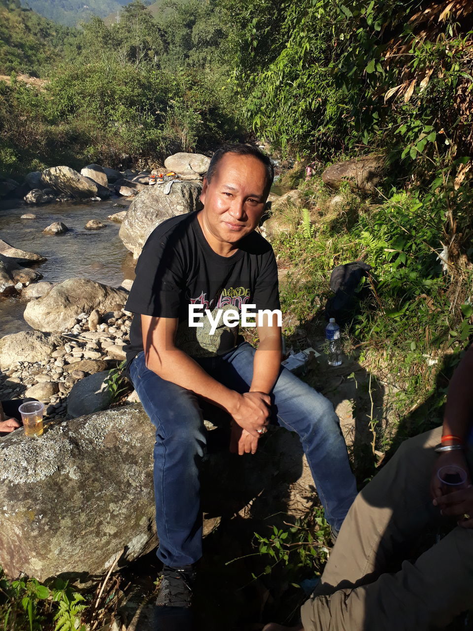 Portrait of smiling man sitting on rock at river