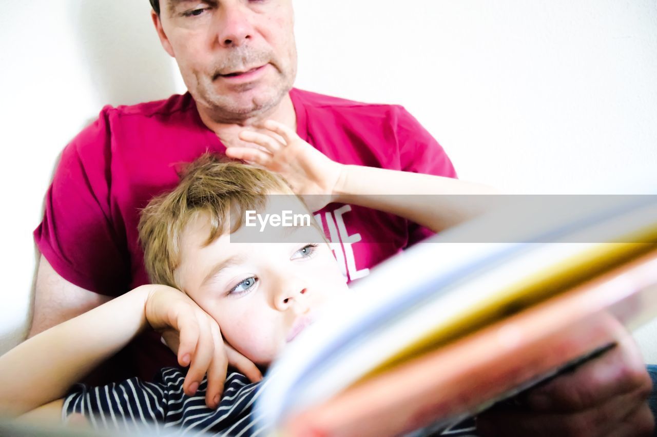 Grandfather and son holding book against white wall