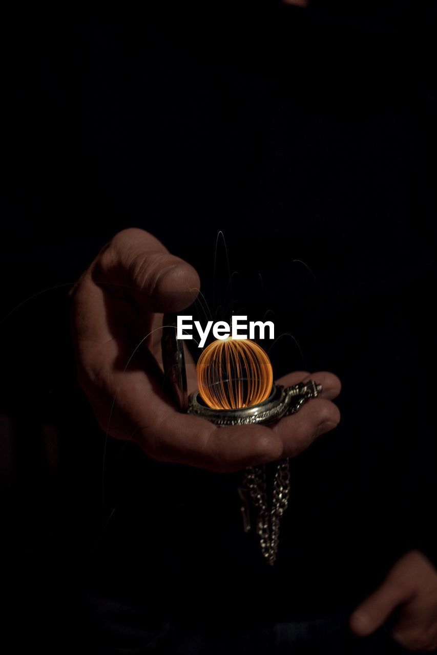 Cropped hands of man holding pocket watch with wire wool against black background