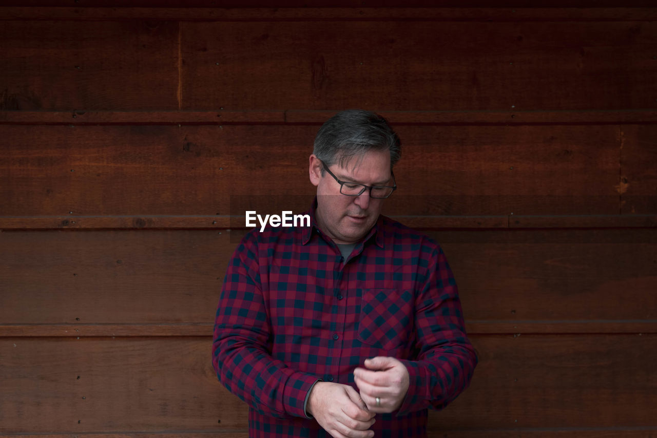 Mature man standing against wooden wall