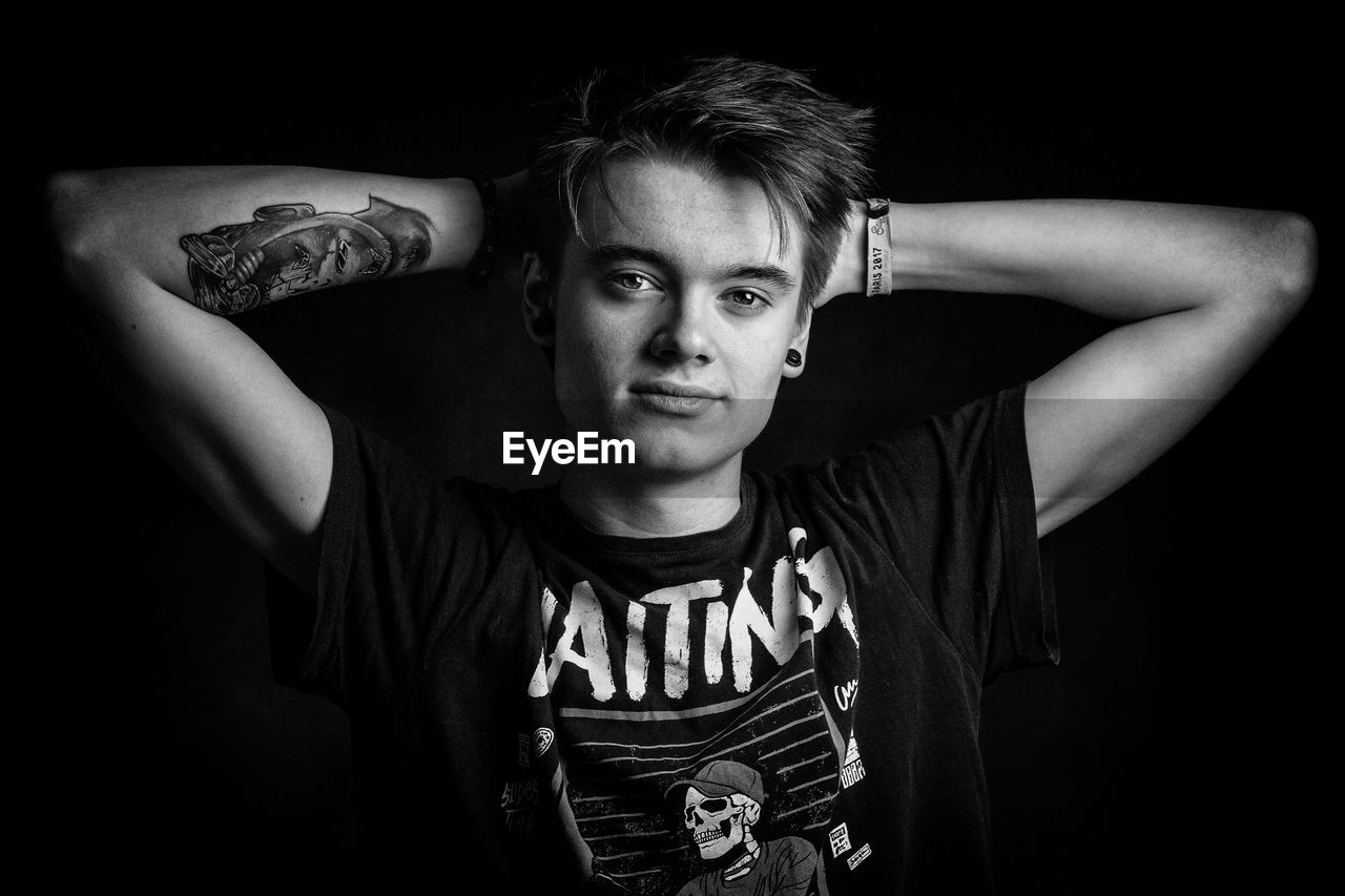 Portrait of young man standing against black background