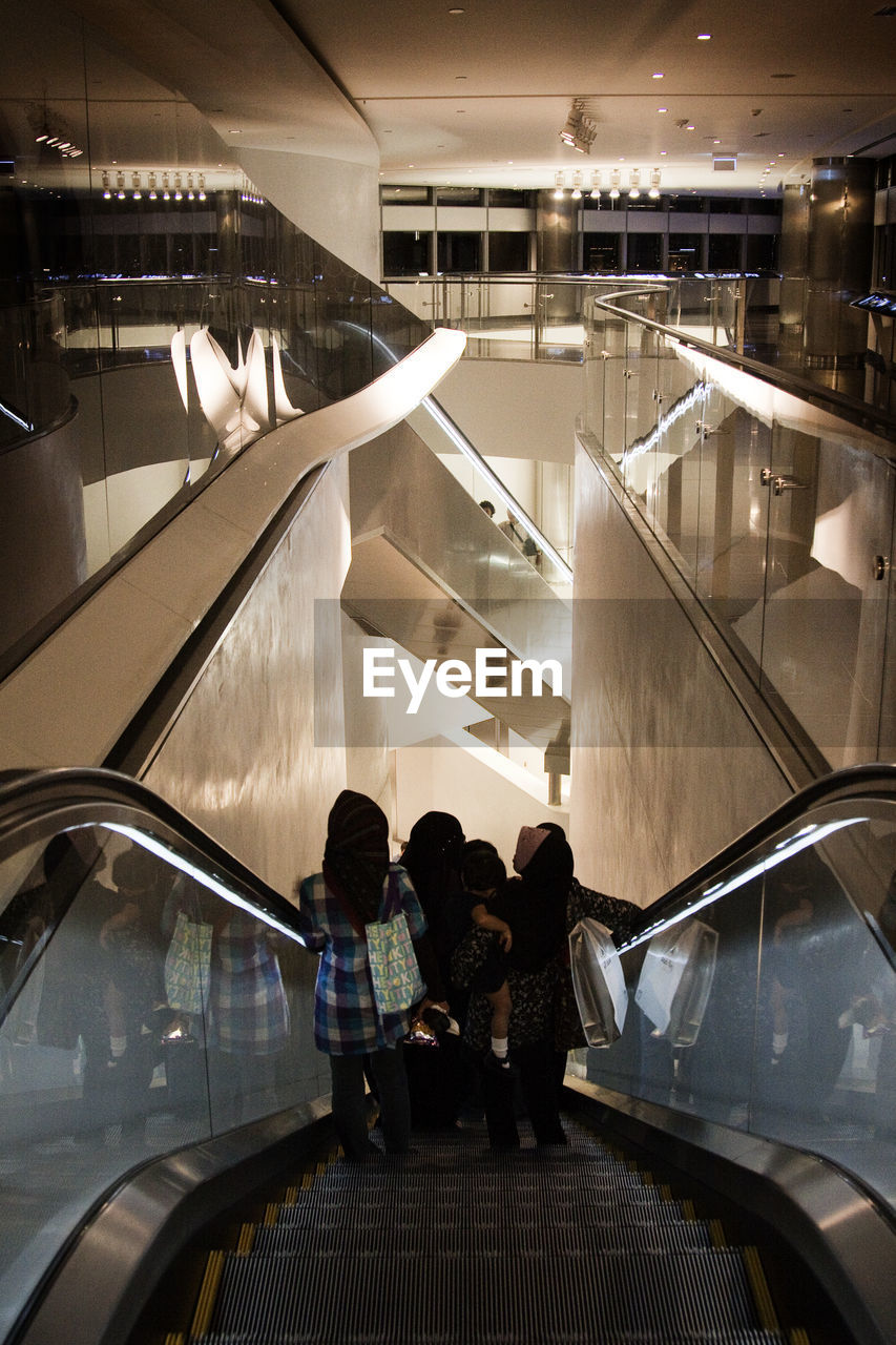 REAR VIEW OF PEOPLE STANDING BY ESCALATOR
